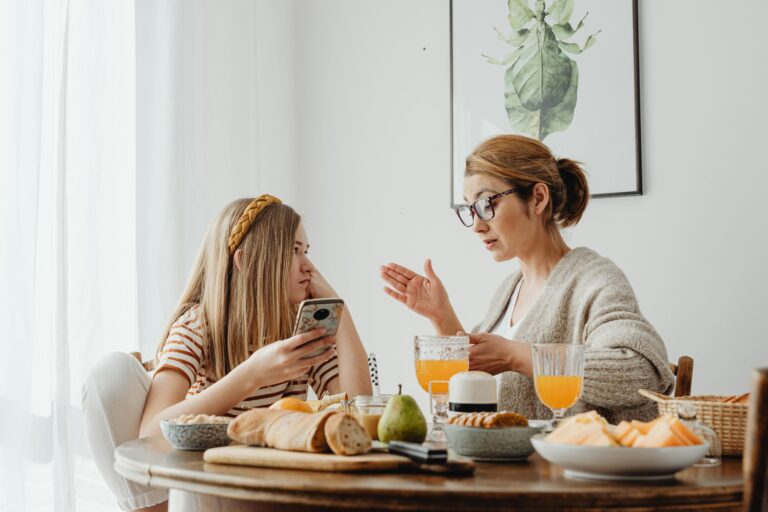 Mother and daughter enjoying breakfast with fresh juice and pastries at home.